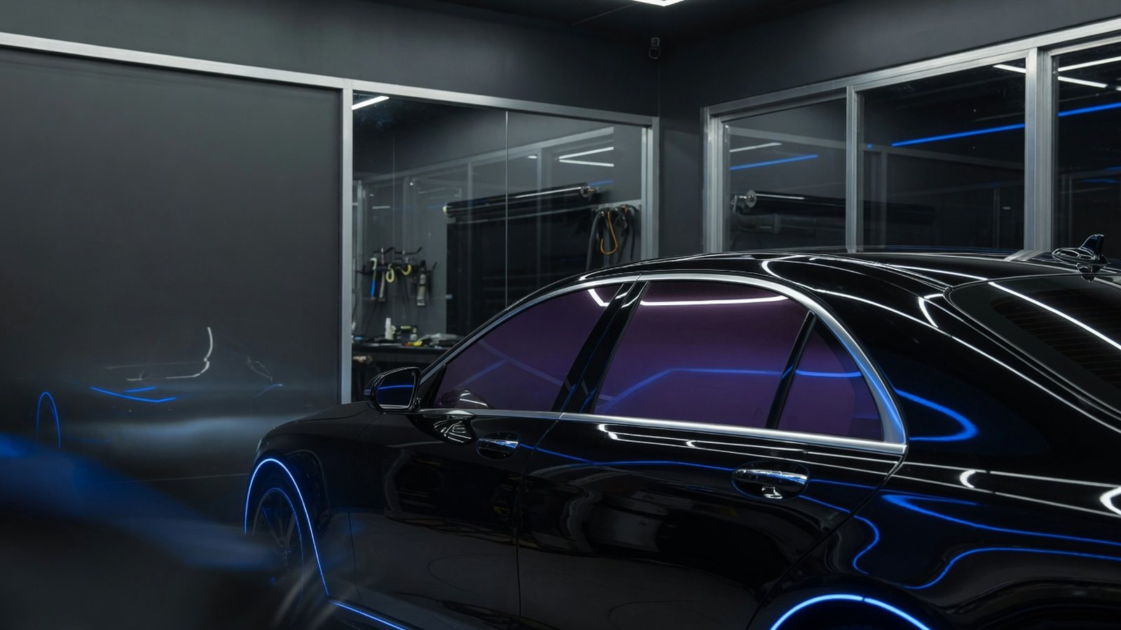 Glossy dark sedan with freshly tinted side glass inside a premium automotive tint shop